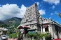 Hindu-Tempel mit detaillierten Verzierungen und bunten Figuren vor einem bewaldeten Berghang.