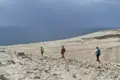 Drei Wanderer auf einem sandigen Küstenpfad. Das Meer ist im Hintergrund sichtbar.