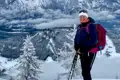 Wanderer mit Rucksack und Wanderstöcken auf einem schneebedeckten Berggipfel.