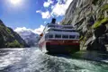 Bei der Reise gleitet Ihr Schiff durch das Wasser, vorbei an hohen Bergen.