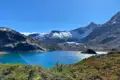 Türkisfarbener Bergsee mit schneebedeckten Bergen und Gletschern im Hintergrund.