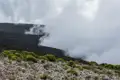 Wolkenverhangener Berghang mit Vegetation im Vordergrund.