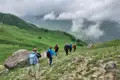 Wanderer auf einem Bergpfad mit Blick auf ein bewölktes Tal.