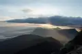 Sonnenstrahlen brechen durch die Wolken über einer Berglandschaft beim Sonnenaufgang.