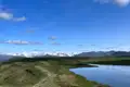 Panoramablick auf einen Wanderweg, der an einem See vorbeiführt, mit schneebedeckten Bergen im Hintergrund.