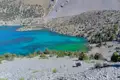 Türkisblauer Bergsee mit Zelten am Ufer und felsiger Umgebung.