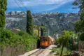 Historische Straßenbahn auf Schienenstrecke inmitten der Landschaft Mallorcas mit Bergen im Hintergrund.