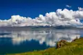 Ruhiger See mit Spiegelung der schneebedeckten Berge und Wolken.