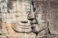Detailansicht eines Steingesichts, das die Verwitterung durch die Zeit zeigt, mit einem weiteren monumentalen Gesicht im Hintergrund.