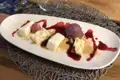 Käsekuchen-Dessert mit Sorbet und Beerensoße, serviert auf einem weißen Teller.