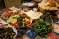 Tisch mit verschiedenen traditionellen Gerichten, wie Salat, Käse, Kräutern und gebratenem Gebäck.