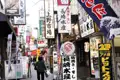 Szene einer belebten Straße in einem japanischen Marktviertel mit Schildern, die für verschiedene Restaurants, darunter "Nagasaki Suisan" (Spezialisiert auf Meeresfrüchte) und "Akebono Steak", werben.
