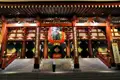 Traditioneller japanischer Tempel mit großer roter Laterne und einer Person, die sich verbeugt.