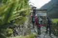 Wandergruppe auf einem Steinpfad in Richtung eines Gästehauses in einer bergigen Landschaft.