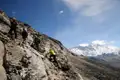 Wanderer beim Aufstieg auf einem felsigen Bergpfad mit Blick auf einen schneebedeckten Gipfel.