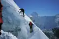 Zwei Bergsteiger mit Seilsicherung beim Aufstieg eines schneebedeckten Grats in den Bergen.
