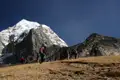 Wanderer auf einem Bergpfad in Richtung eines schneebedeckten Gipfels.