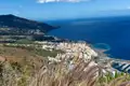 Blick über eine Küstenstadt am Meer mit Hafen und umgebender Berglandschaft.