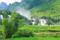 Szenischer Wasserfall umgeben von üppiger Vegetation und Reisfeldern.