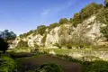 Felsige Landschaft mit Bäumen und Sträuchern sowie landwirtschaftlich genutzten Flächen im Vordergrund.