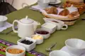 Frühstückstisch mit Teekanne, Brötchenkorb, Marmelade, Butter, Sahne und Schokocreme.