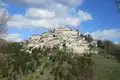 Panoramablick auf ein italienisches Bergdorf, umgeben von bewaldeten Hügeln.