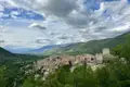 Panoramablick auf ein italienisches Bergdorf mit umliegenden Bergen und Bäumen.