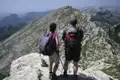 Zwei Wanderer mit Wanderstöcken stehen auf einem Berggipfel und schauen auf das Panorama.