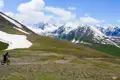 Mountainbiker auf einem Bergpfad mit Schnee und Bergen im Hintergrund.