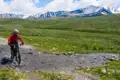 Mountainbiker durchquert einen Bach im Hochgebirge vor der Kulisse schneebedeckter Gipfel.
