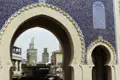 Blick durch ein verziertes Tor in Fes auf die dahinterliegende Moschee und den Markt.