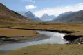 Flusslandschaft in den Bergen mit schneebedeckten Gipfeln im Hintergrund.