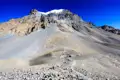 Schneebedeckter Berggipfel und Wanderer auf einem steinigen Pfad.
