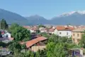 Panoramablick auf eine Stadt in einem Tal, umgeben von bewaldeten Hügeln und schneebedeckten Bergen.