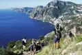 Wanderer mit Rucksäcken auf einem Bergpfad mit Blick auf die Küste und das tiefblaue Meer.