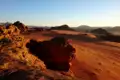 Panorama der Wüste mit Sanddünen, Felsformationen und einem Camp im Hintergrund.