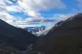 Gebirgstal mit Fluss und schneebedeckten Gipfeln im Hintergrund.