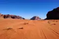 Offroad-Spuren durch die roten Sanddünen einer Wüste, umgeben von markanten Felsformationen.