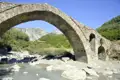 Alte Steinbrücke über einen Fluss, umgeben von Bergen.