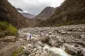 Wanderer überquert eine provisorische Brücke über einen Fluss im Gebirge.