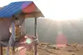 Eine Buddha-Statue unter einem Schutzdach mit Blick auf einen sonnigen Berghang.