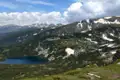 Zwei Bergseen inmitten einer grünen Landschaft mit schneebedeckten Gipfeln im Hintergrund.