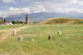Burana-Turm in Kirgisistan mit Steinen und Hügeln im Vordergrund und Bergen im Hintergrund.