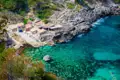 Kleine Bucht mit Gebäuden und kristallklarem, türkisfarbenem Wasser.