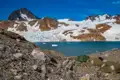 Campingplatz mit Zelten am Ufer eines türkisfarbenen Gletschersees, umgeben von einem Gletscher und schneebedeckten Bergen.