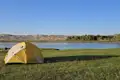 Campingplatz am Fluss mit Zelt und Hügeln im Hintergrund.