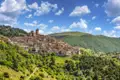 Panoramablick auf ein italienisches Bergdorf mit umliegenden Hügeln und bewaldetem Gelände.