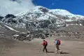 Zwei Wanderer auf einer Bergwanderung nähern sich einem schneebedeckten Gipfel.