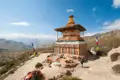 Traditioneller Stupa mit bunten Streifen und Gebetsfahnen in einer Bergregion.