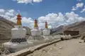 Weiße Stupas mit bunten Verzierungen und schneebedeckte Berge im Hintergrund.